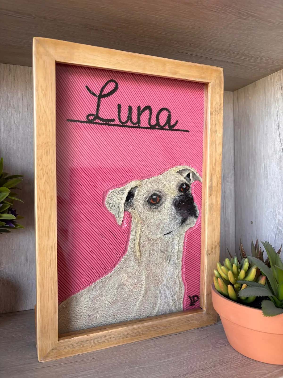 Cuadro en plastilina y en relieve de Luna, una perra blanca, sobre fondo rosado, con marco de madera