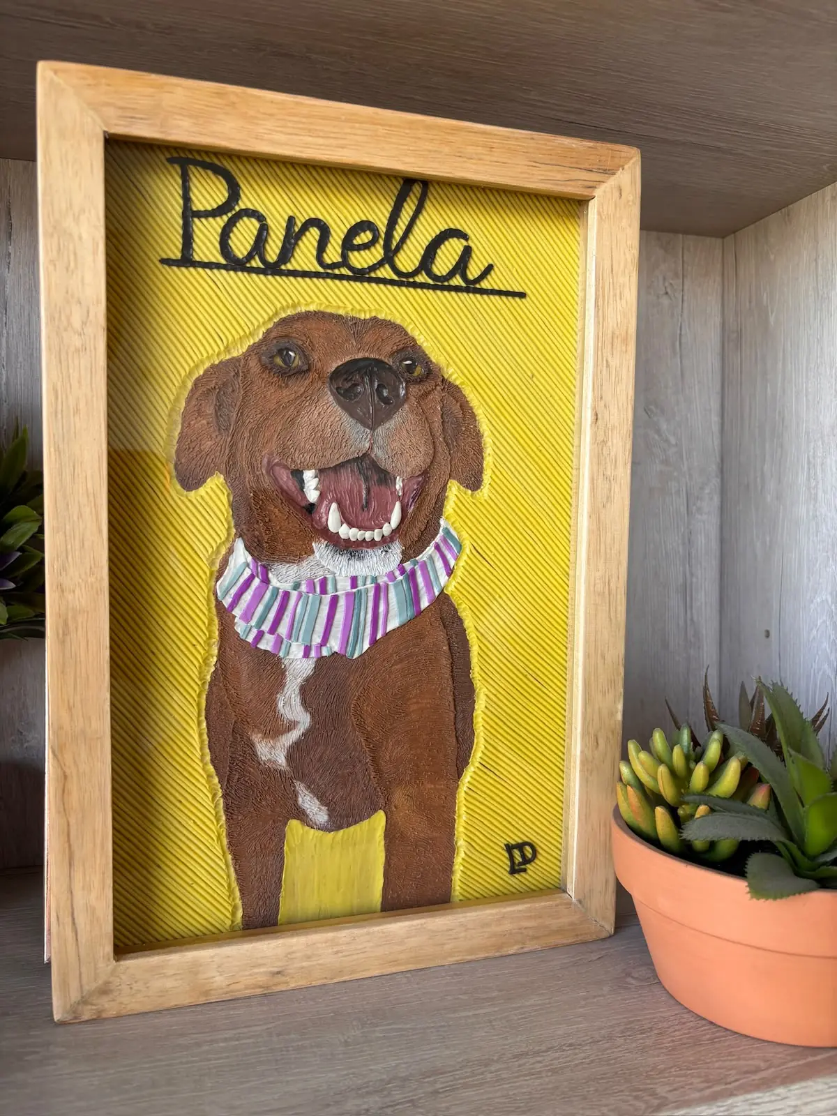 Cuadro en plastilina y en relieve de Panela, una perra café sonriente con pañoleta, sobre fondo amarillo