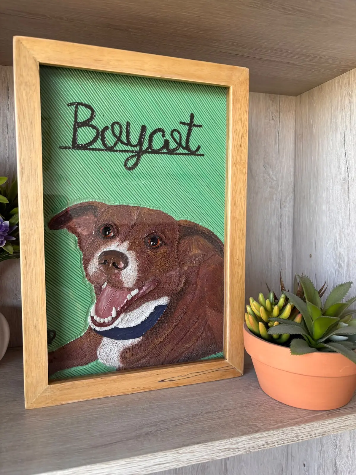 Cuadro en plastilina y en relieve de un perro café con collar, con su nombre escrito, sobre fondo verde