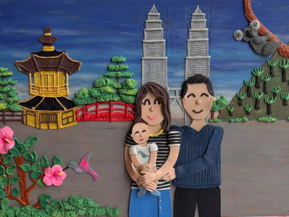 Retrato familiar en plastilina y en relieve: una pareja con su bebé en brazos, frente a una pagoda, las Torres Petronas y un koala